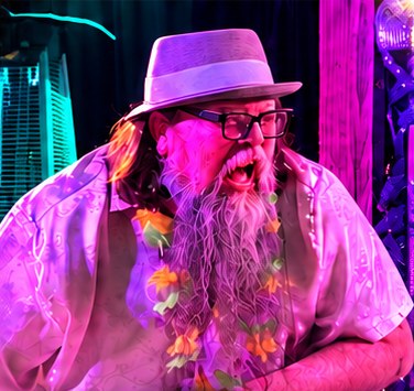 Otis Walker performing at the keys in a fedora, lit in pink and violet stage light